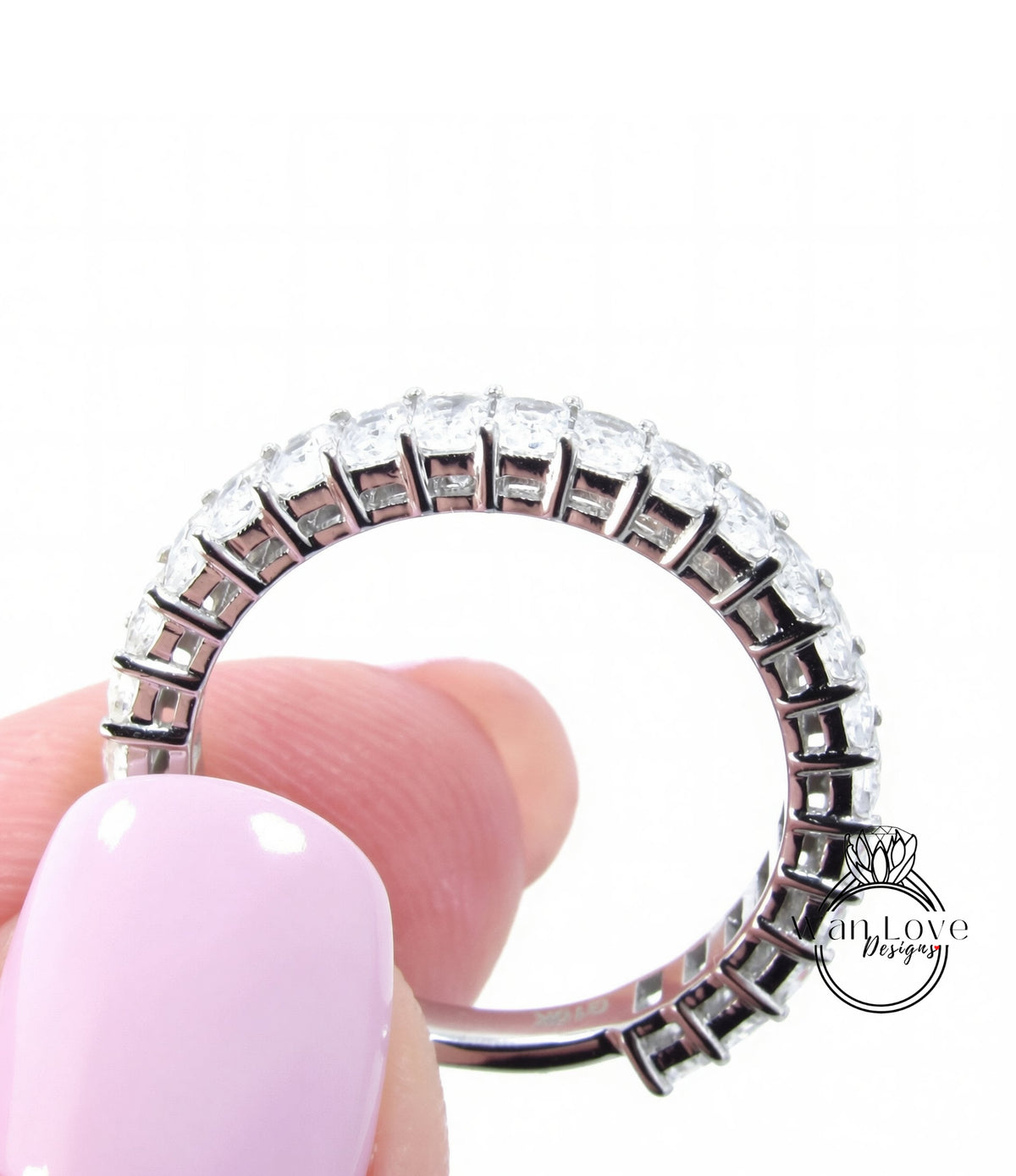 A close-up of a person's hand holding a ring with a row of diamonds on the band.