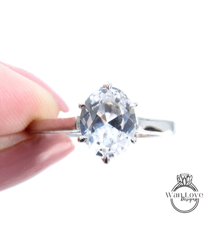 A close-up of a person's hand holding a diamond ring with a large, clear gemstone.