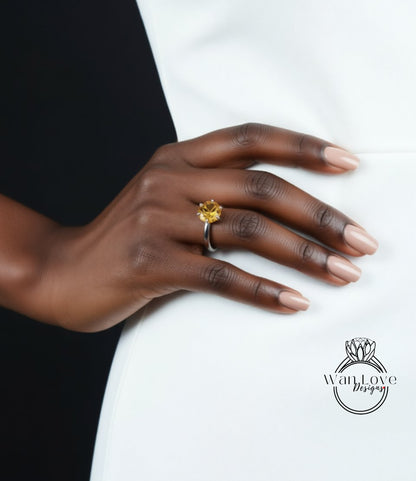 A close-up of a hand wearing a ring with a yellow gemstone, resting on a white surface.