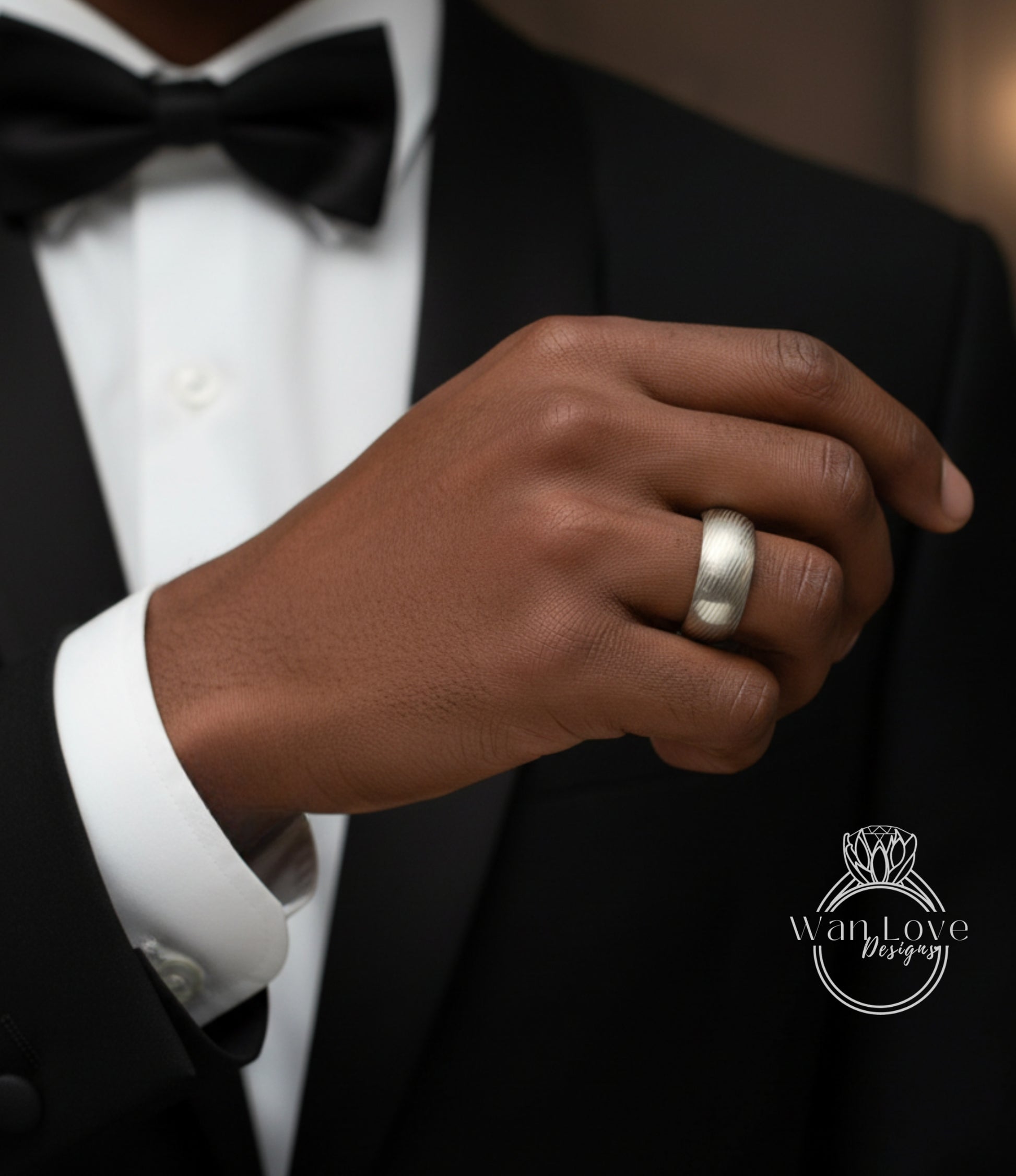 A close-up of a person's hand wearing a black tuxedo and a silver ring on the ring finger.