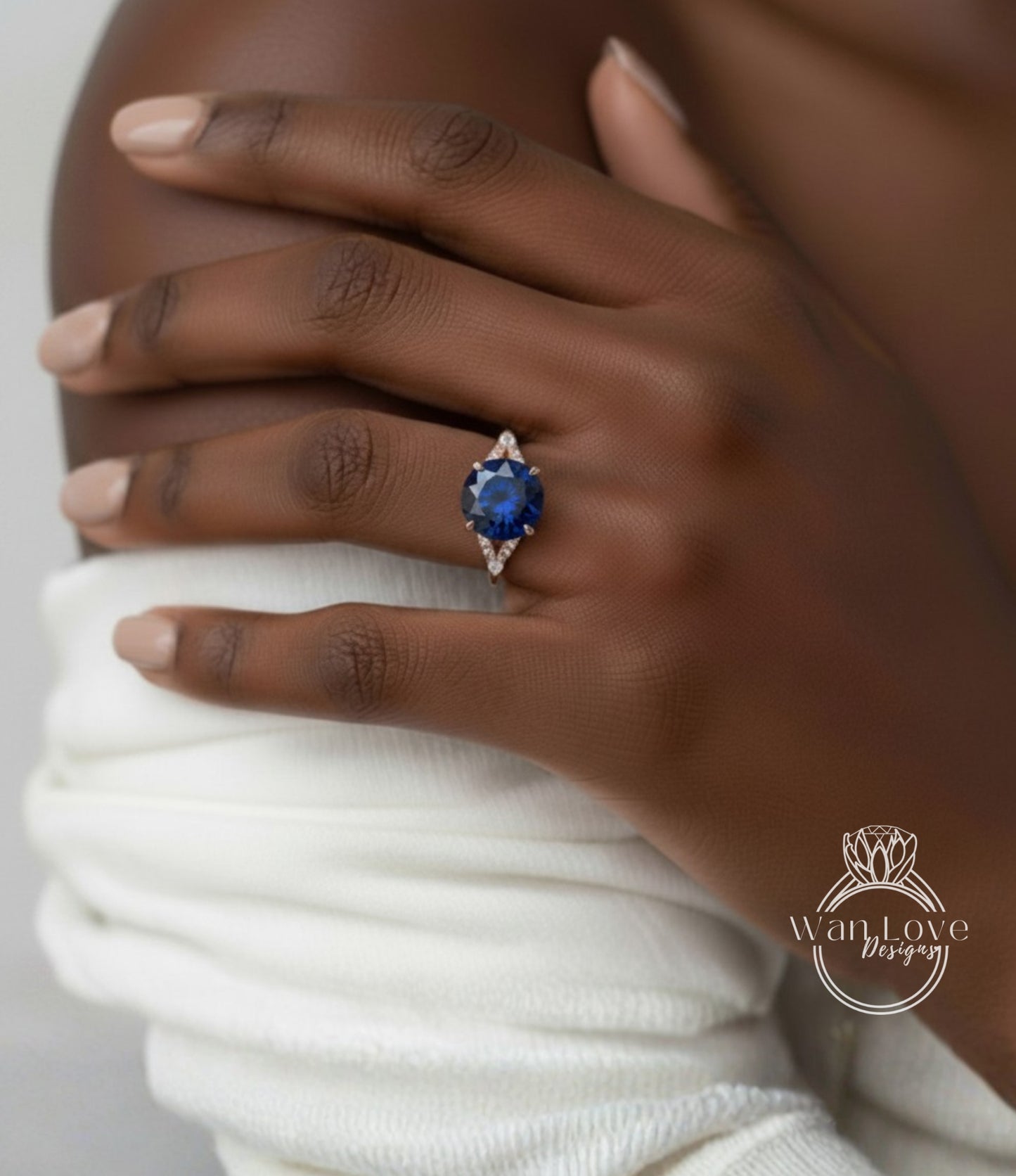 A close-up of a hand wearing a ring with a blue gemstone, resting on a white fabric.