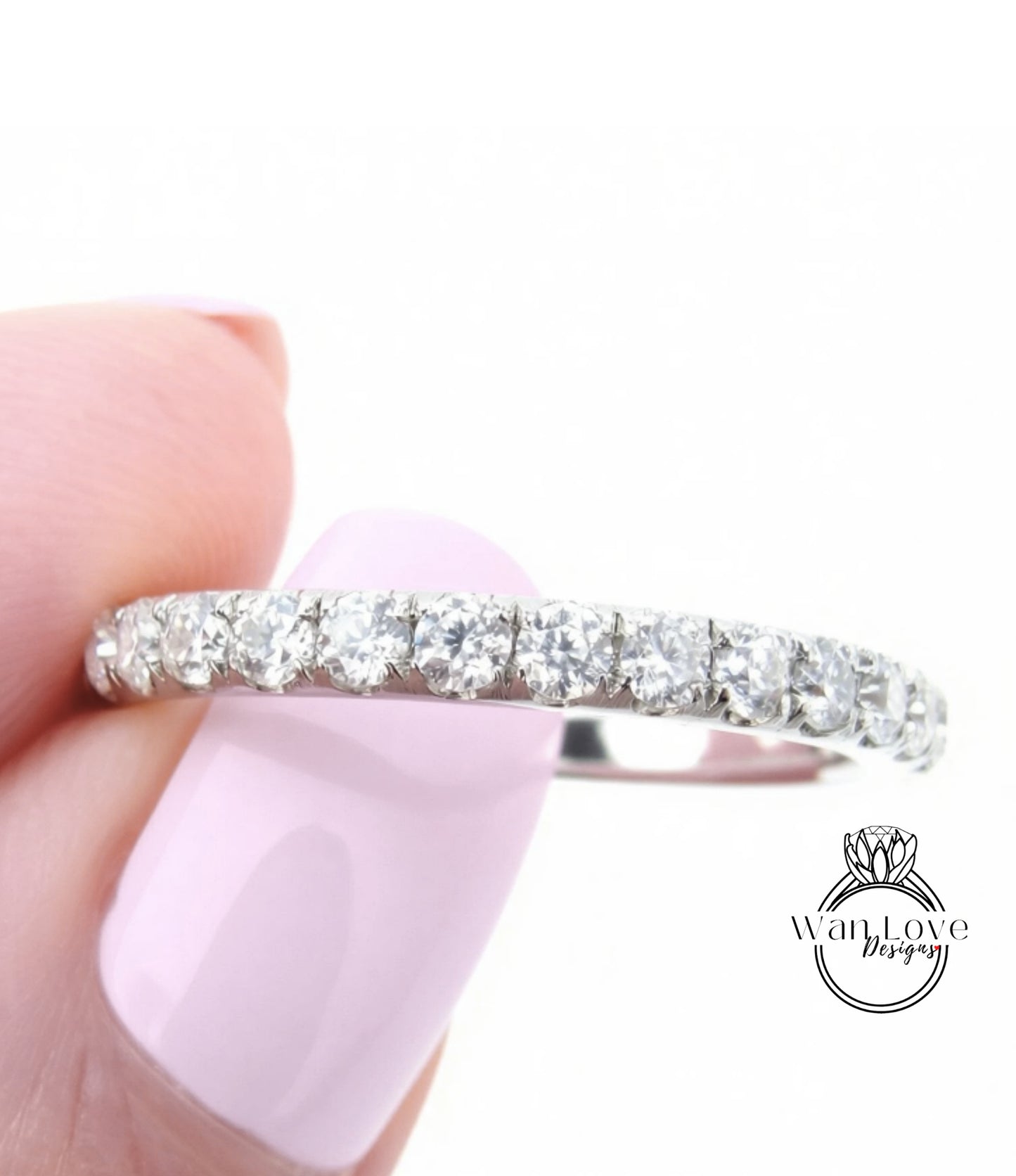 A close-up of a person's hand holding a diamond band ring with a row of clear diamonds on the band.