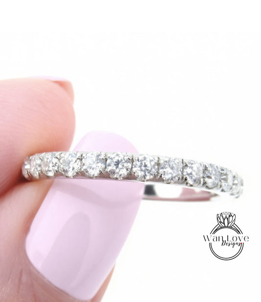 A close-up of a person's hand holding a diamond band ring with a row of clear diamonds on the band.