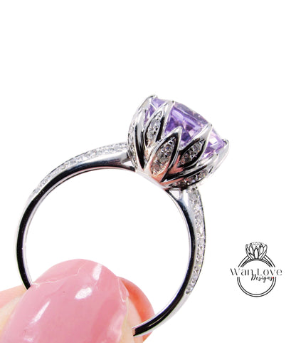 A close-up of a silver ring with a large purple gemstone, held in a person's hand against a white background.