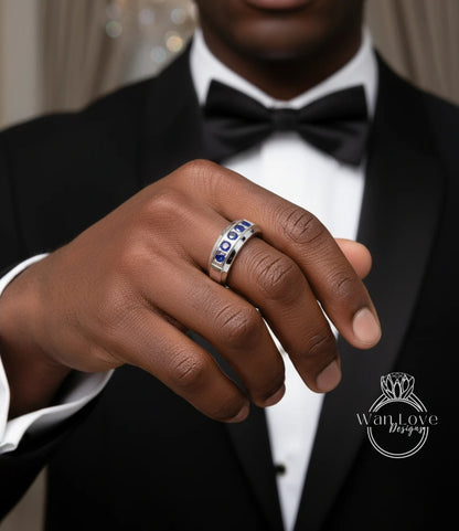 A close-up of a person's hand wearing a ring with blue gemstones, wearing a black tuxedo with a bow tie.