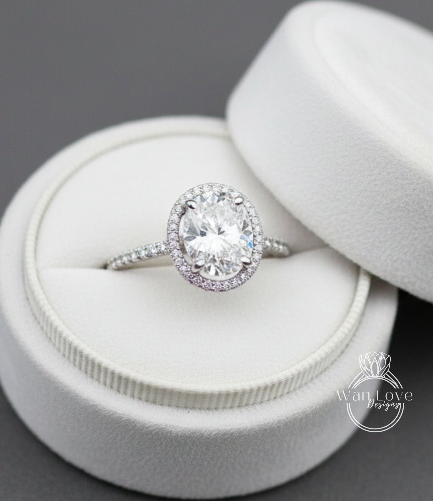 A large oval-shaped diamond ring with a halo of smaller diamonds set in a white velvet box.