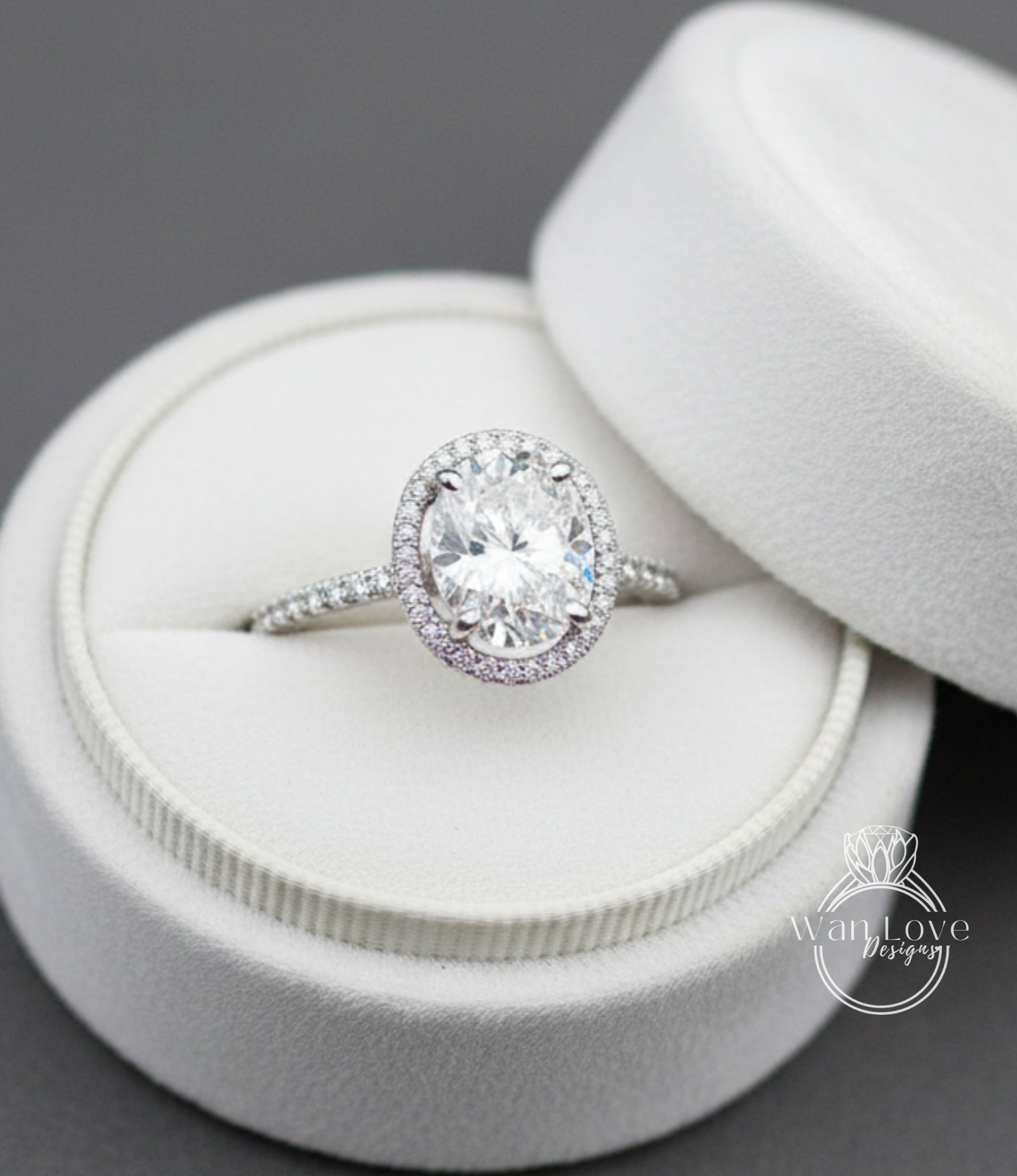 A large oval-shaped diamond ring with a halo of smaller diamonds set in a white velvet box.