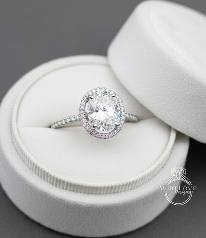 A large oval-shaped diamond ring with a halo of smaller diamonds set in a white velvet box.
