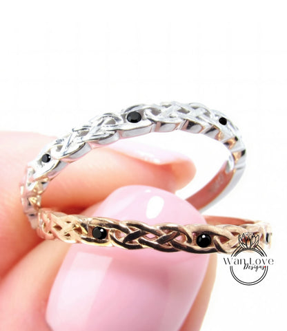 A close-up image of a person's hand holding two rings, one silver and one gold, with intricate designs and black stones.