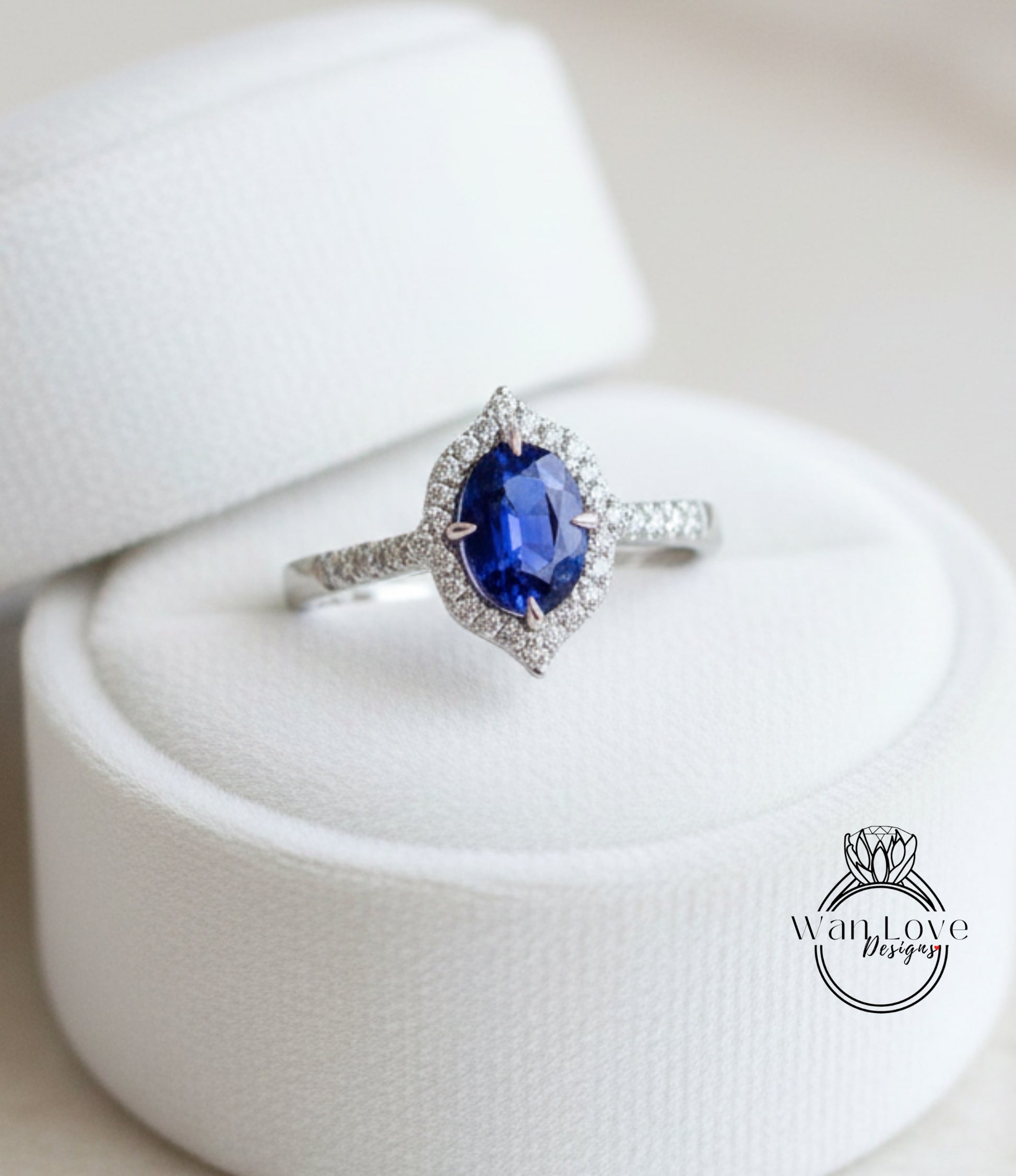 A diamond engagement ring with a large oval-shaped blue gemstone set in a halo of smaller diamonds, displayed in a white jewelry box.