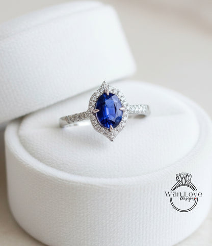 A diamond engagement ring with a large oval-shaped blue gemstone set in a halo of smaller diamonds, displayed in a white jewelry box.