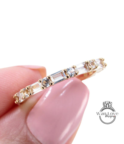 A close-up image of a person's hand holding a gold ring with clear gemstones.