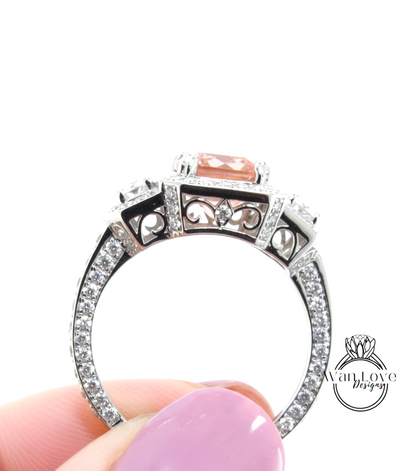 A close-up of a person's hand holding a silver ring with a pink gemstone and intricate designs.
