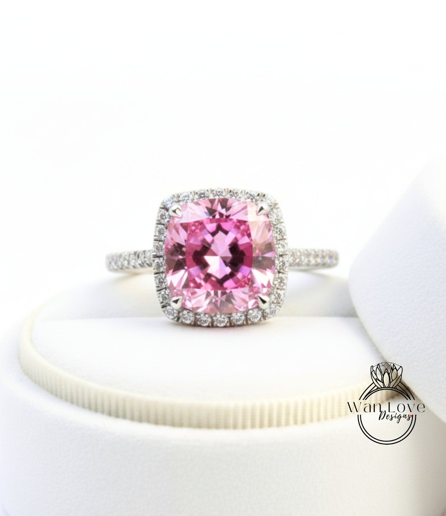 A close-up image of a pink gemstone ring with a halo of diamonds around it, placed on a white surface.