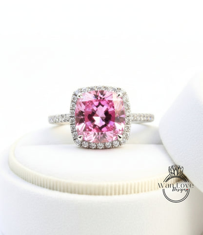 A close-up image of a pink gemstone ring with a halo of diamonds around it, placed on a white surface.