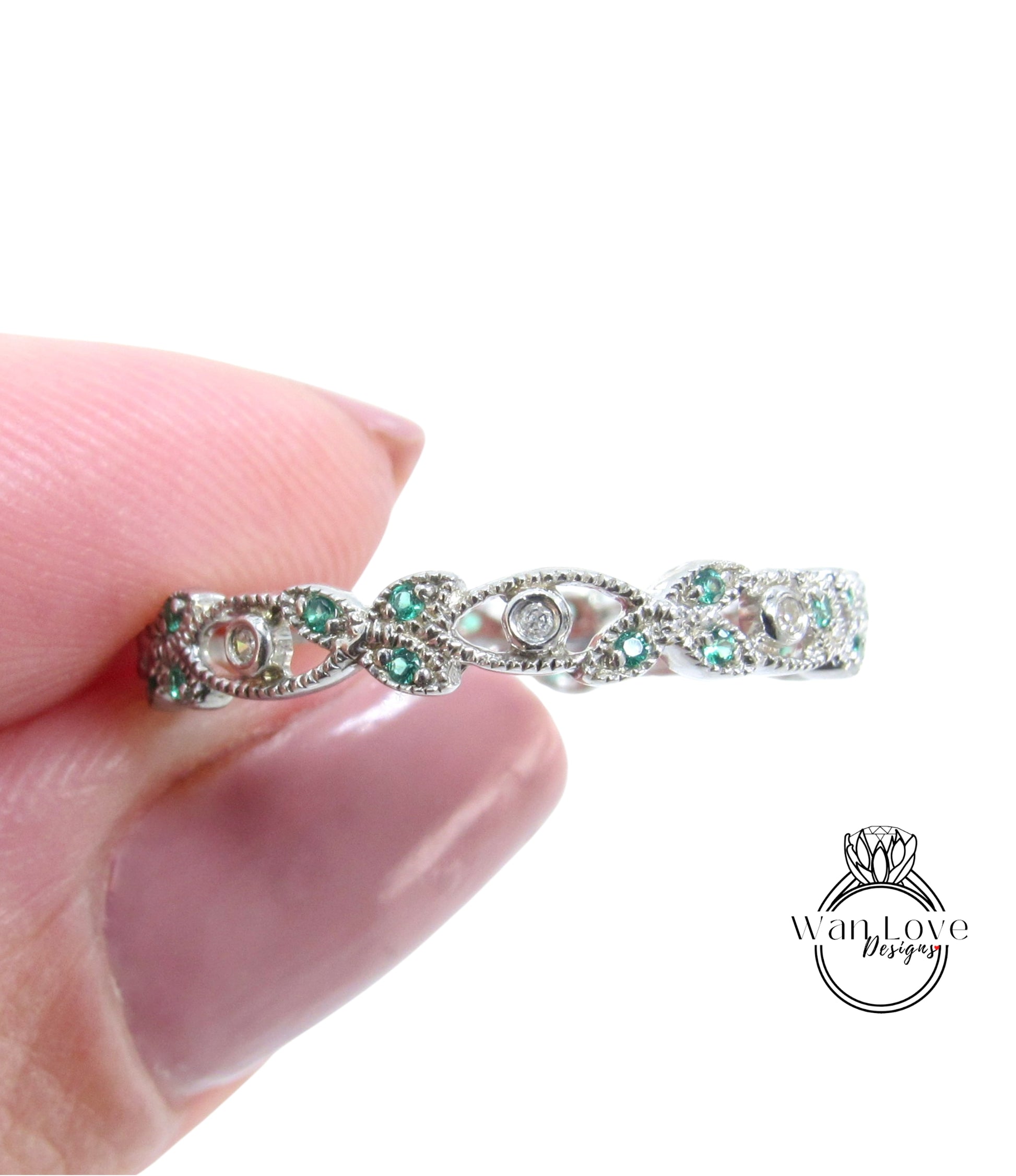 A close-up image of a person's hand holding a silver ring adorned with green gemstones.