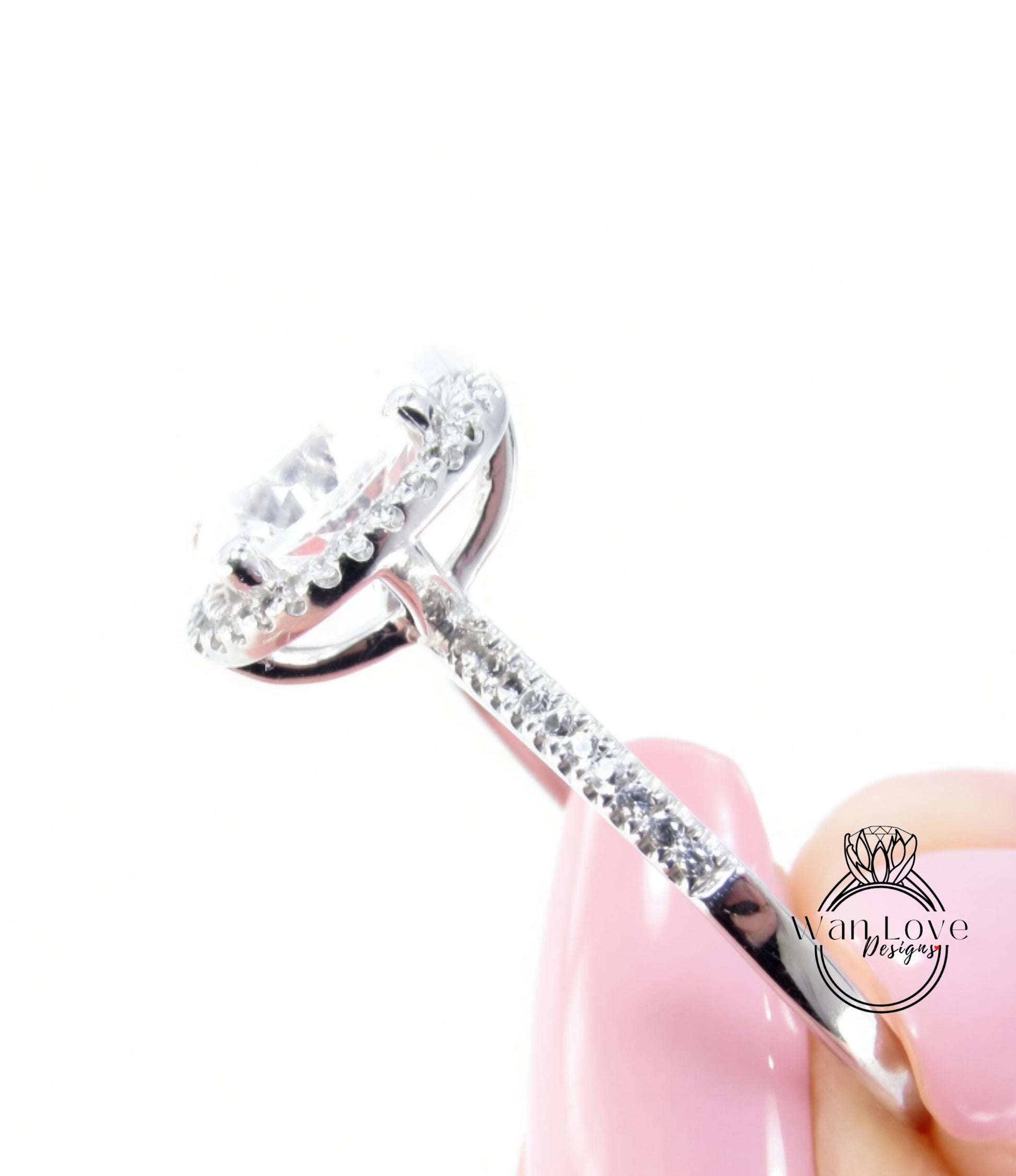 A close-up view of a diamond engagement ring being held by a person's hand, with the ring's halo and band visible.