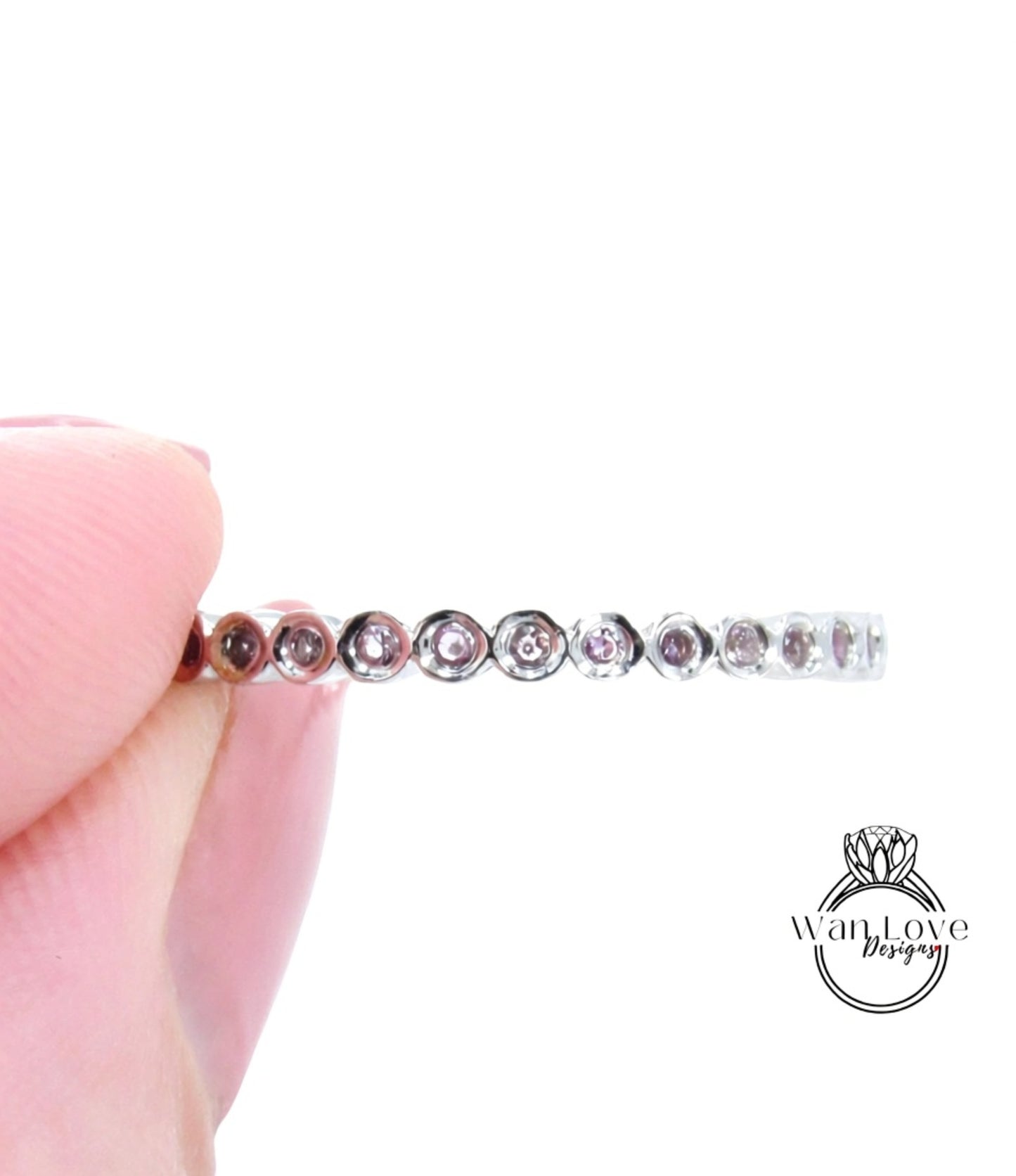 A close-up image of a person's hand holding a ring with a row of small diamonds on it.