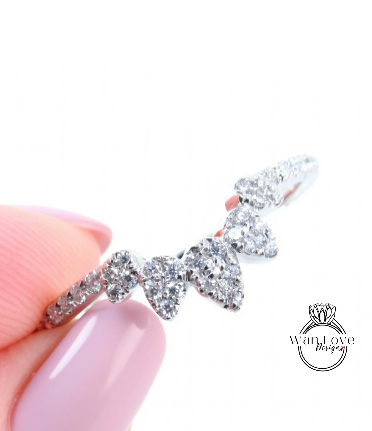 A close-up of a person's hand holding a silver ring with a row of small diamonds on it.