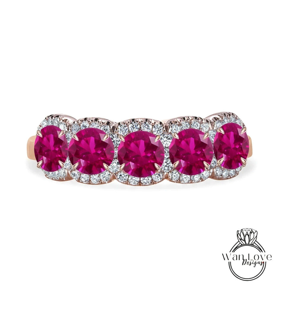 A pink gemstone ring with a row of five large, round, deep red gemstones set in a halo of smaller diamonds.