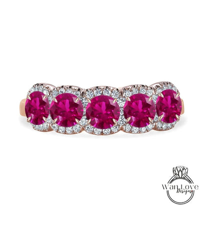 A pink gemstone ring with a row of five large, round, deep red gemstones set in a halo of smaller diamonds.
