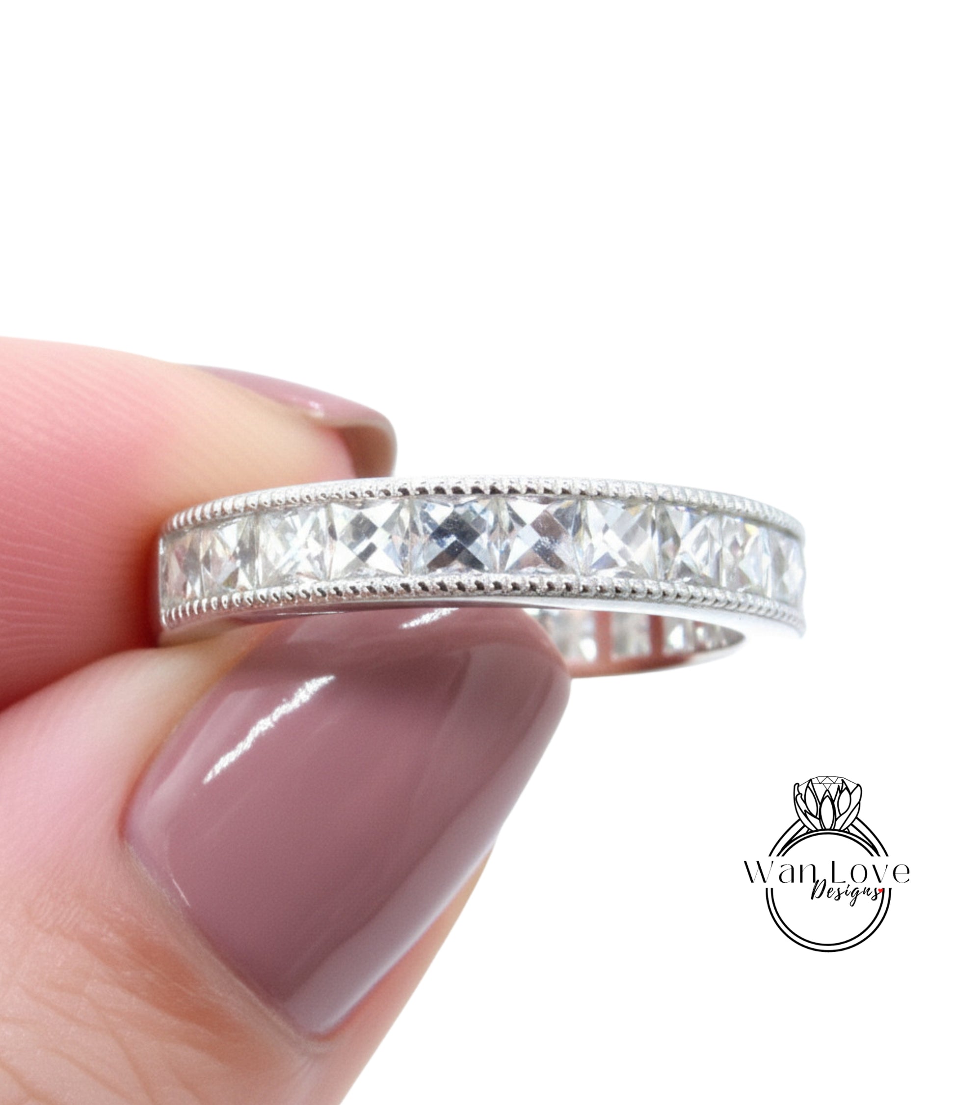 A close-up image of a person's hand holding a silver ring with a row of clear gemstones.