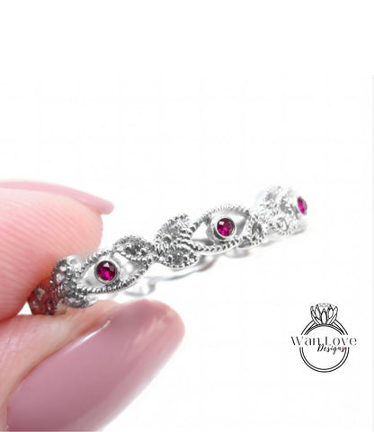 A hand holding a silver ring with a decorative design and red gemstones.