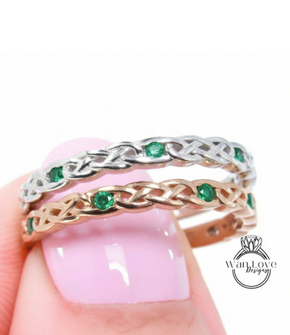 A close-up of a person's hand wearing a silver and gold ring with green gemstones.