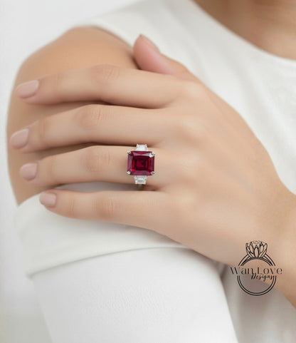 A close-up of a person's hand wearing a large, red gemstone ring on the ring finger.