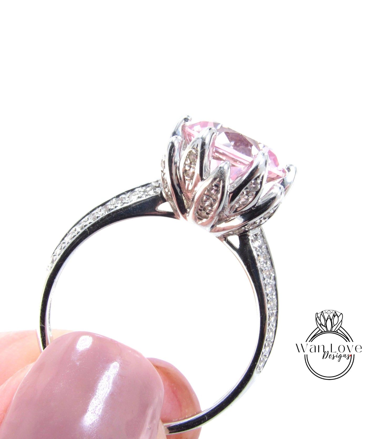 A close-up of a silver ring with a large pink gemstone, held in a person's hand.