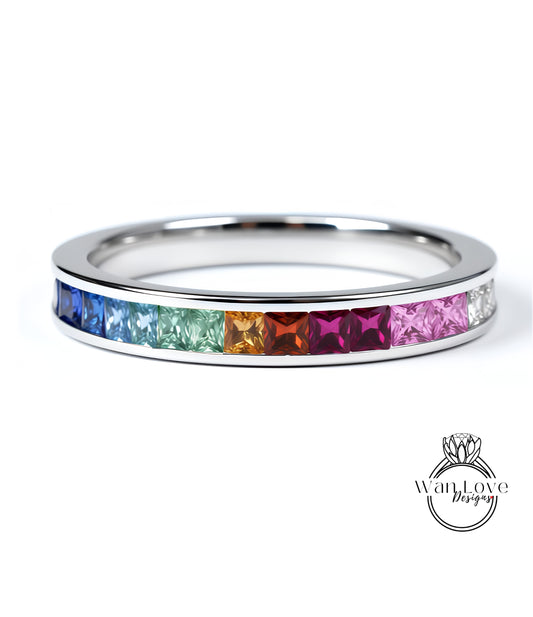 A silver ring with a row of colorful gemstones, including blue, green, orange, pink, and purple stones, arranged in a rainbow-like pattern.