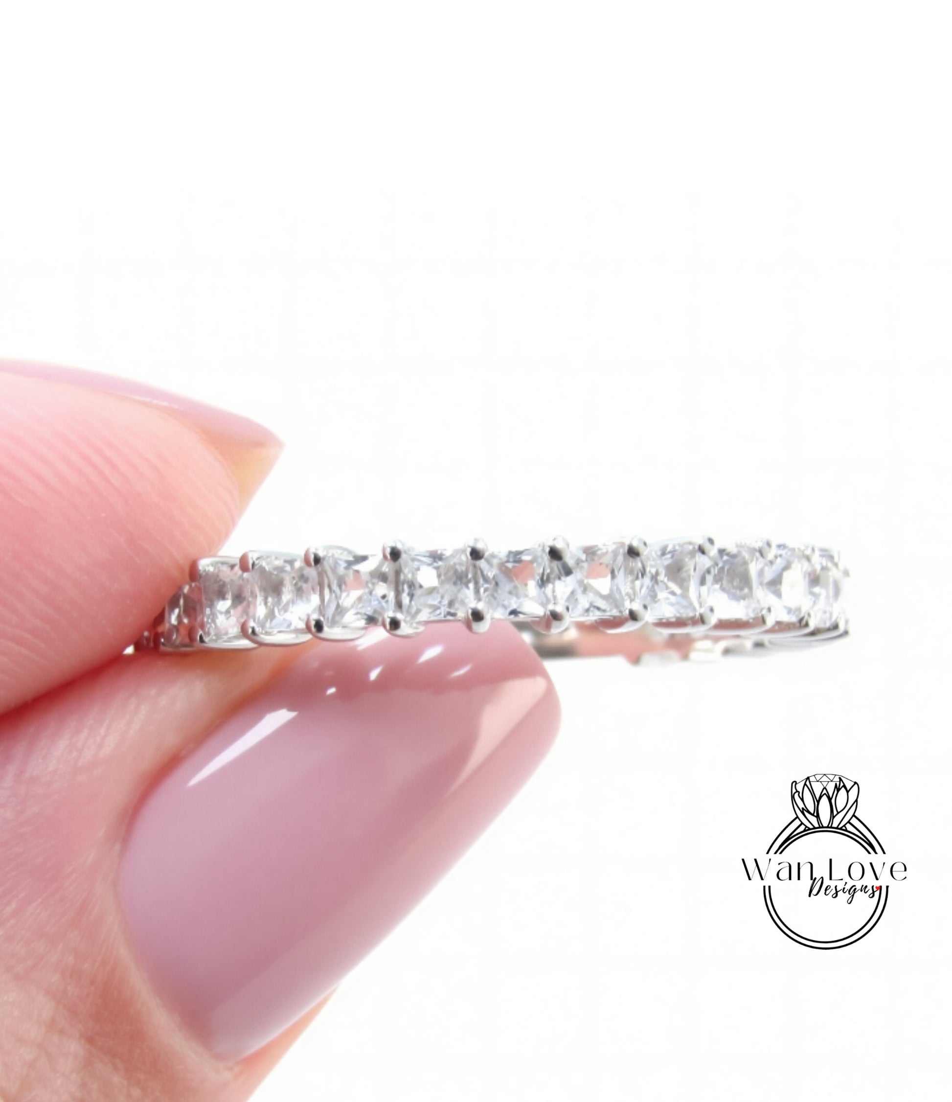 A close-up of a person's hand holding a silver ring with a row of clear gemstones.