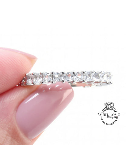 A close-up of a person's hand holding a silver ring with a row of clear gemstones.