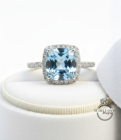 A stunning blue gemstone ring with a halo of diamonds, displayed on a white surface.