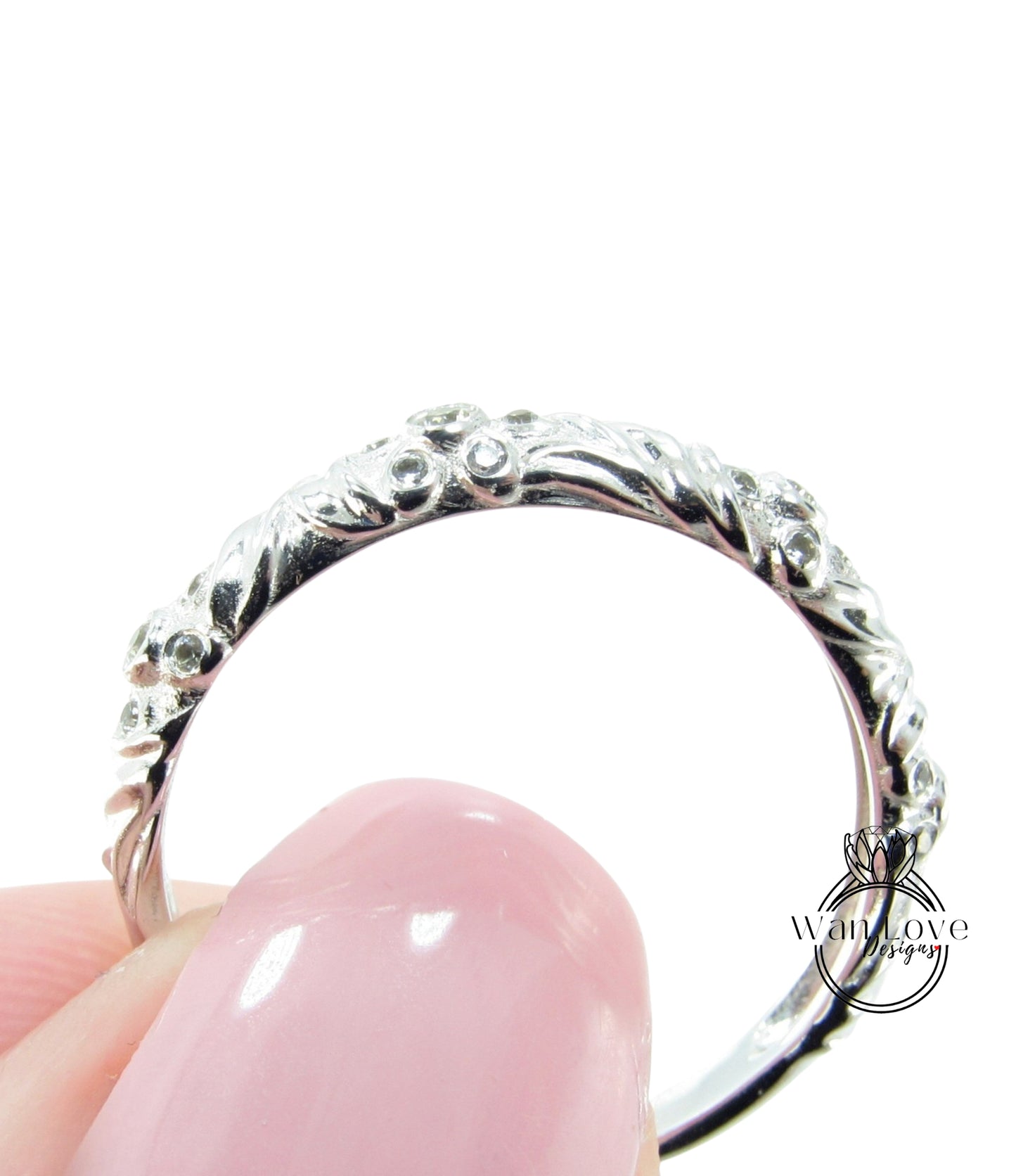 A close-up image of a person's hand holding a silver ring with an intricate floral design.