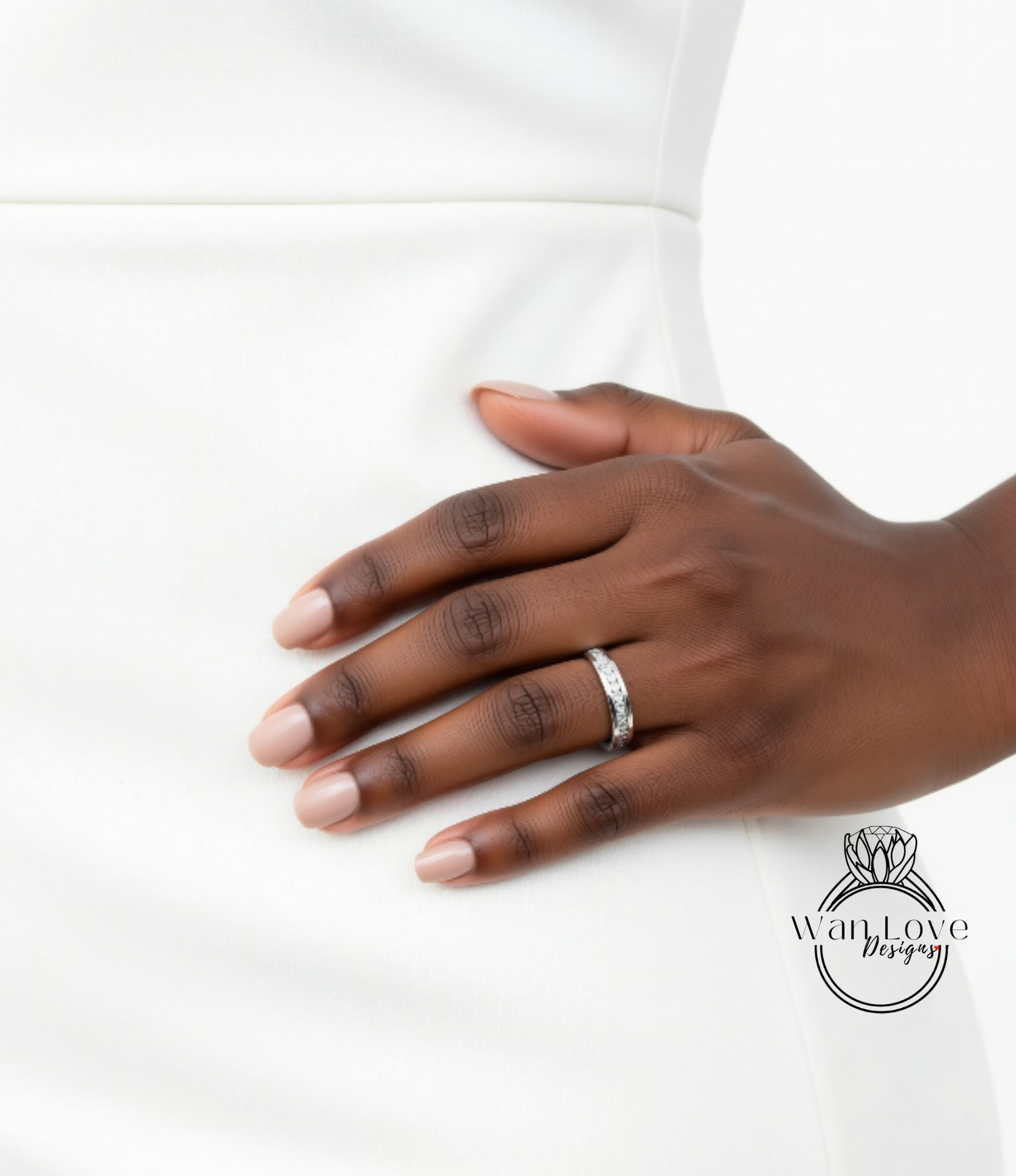 A close-up of a hand wearing a ring on the ring finger, with a white dress visible in the background.