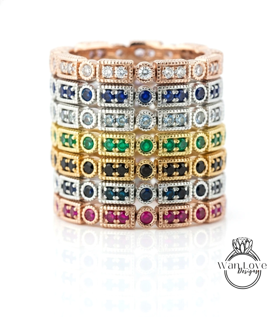 A stack of rings with various colored gemstones, including diamonds, set in a rose gold or silver metal.