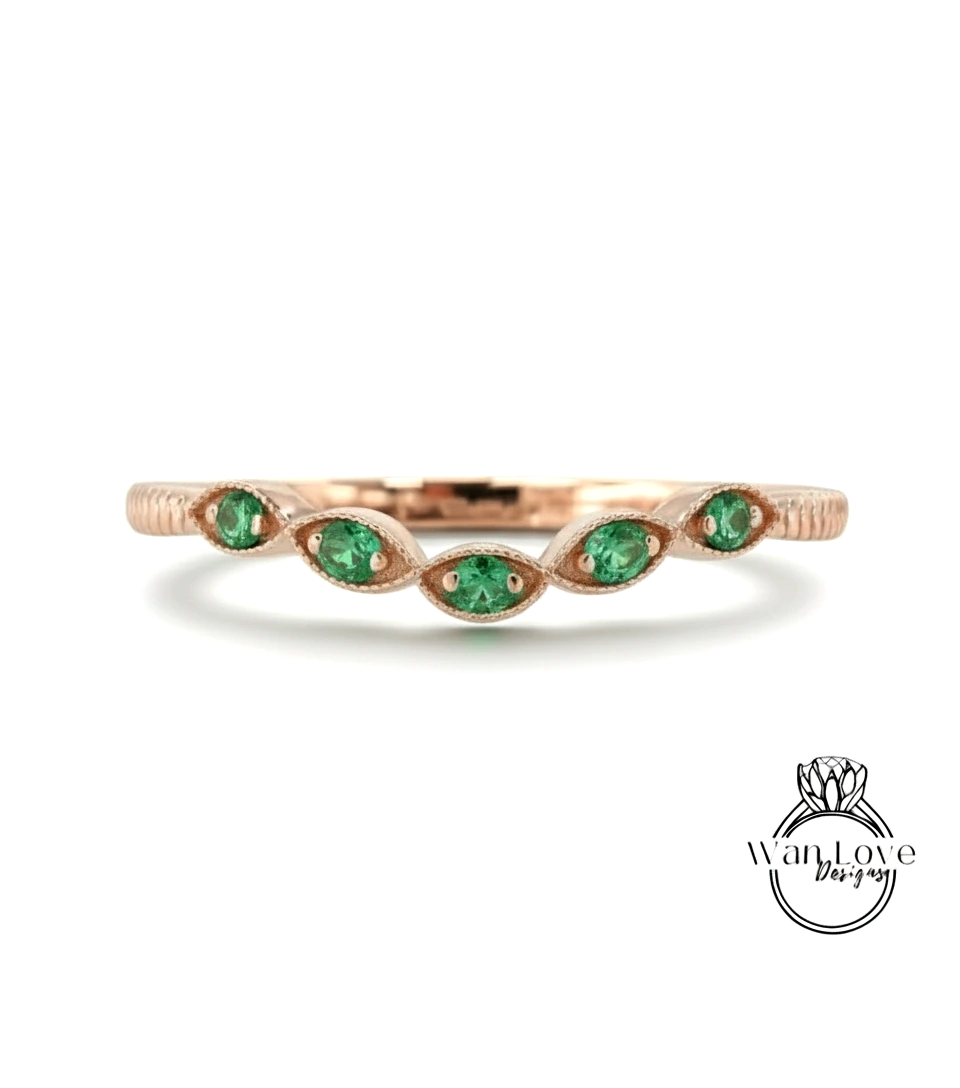 A rose gold ring with a row of green gemstones, likely emeralds, set in the center.