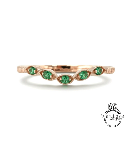 A rose gold ring with a row of green gemstones, likely emeralds, set in the center.