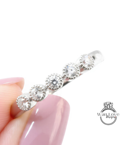 A close-up image of a person's hand holding a silver ring with a row of small diamonds on it.