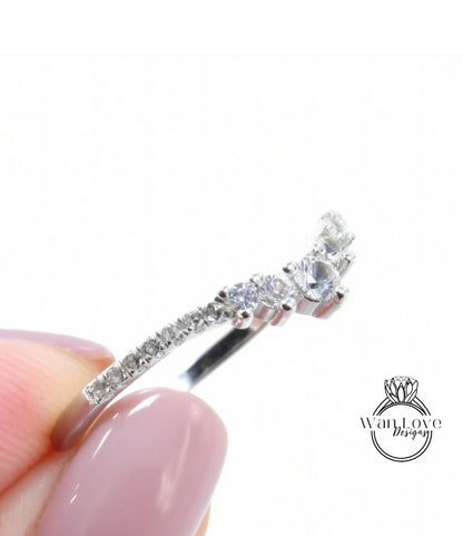 A close-up view of a person's hand holding a silver ring with a row of small diamonds on the band.