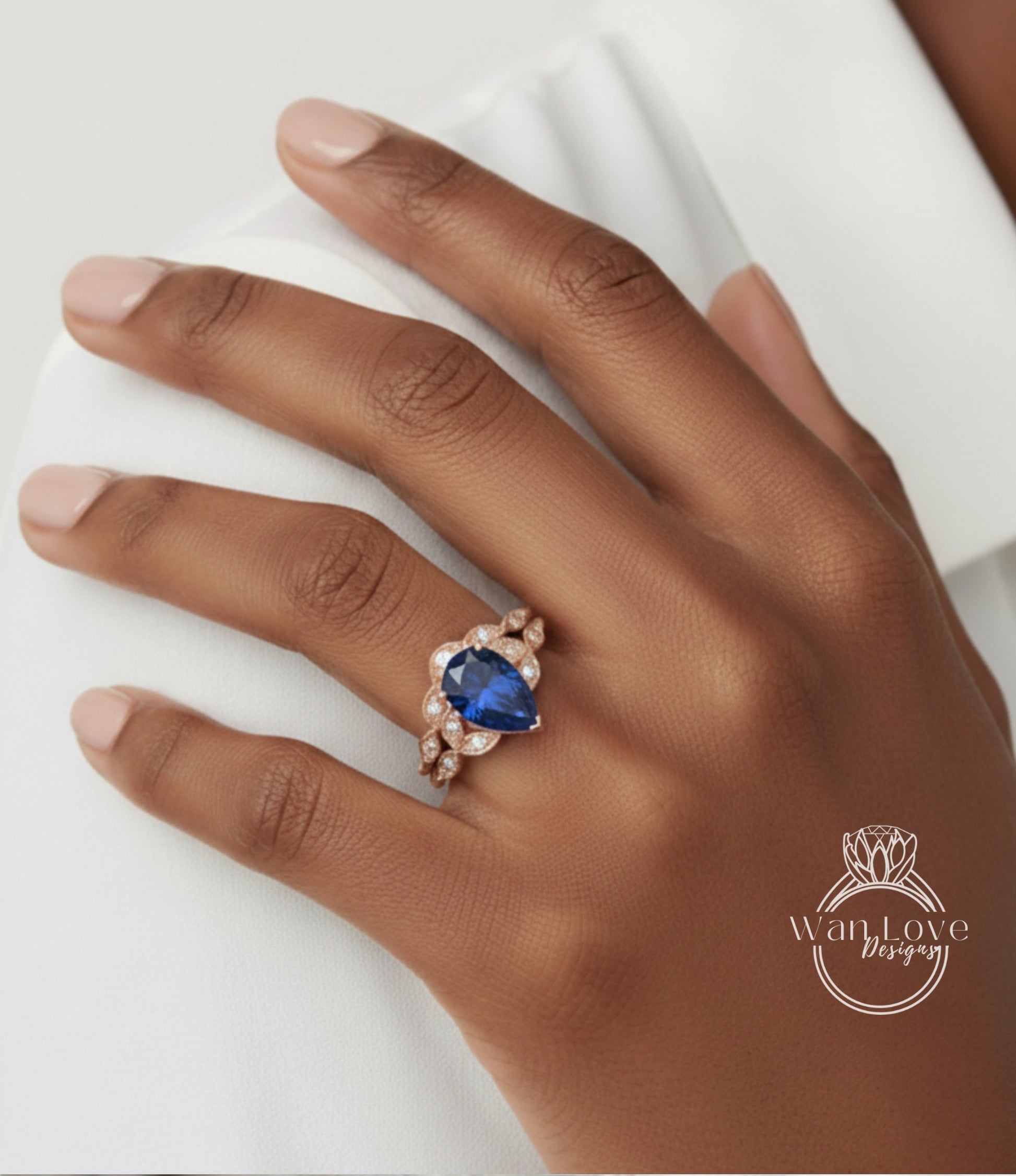 A close-up of a hand wearing a gold ring with a blue gemstone, resting on a white surface.