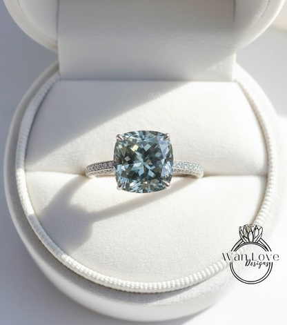 A large, blue-green gemstone engagement ring is displayed in a white jewelry box, showcasing its intricate design and sparkling details.