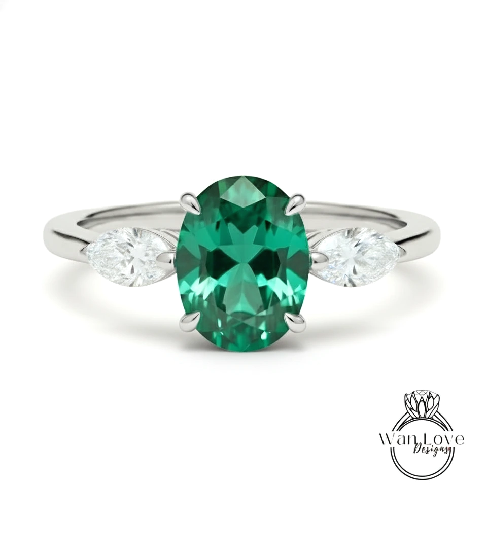 A silver ring with a large oval-shaped green gemstone in the center, flanked by two smaller diamonds on either side.