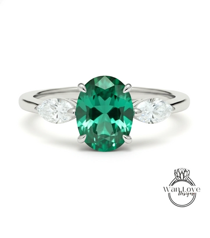 A silver ring with a large oval-shaped green gemstone in the center, flanked by two smaller diamonds on either side.