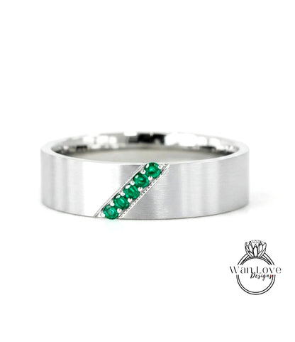 A silver ring with a diagonal line of green gemstones, likely emeralds, set in the center.