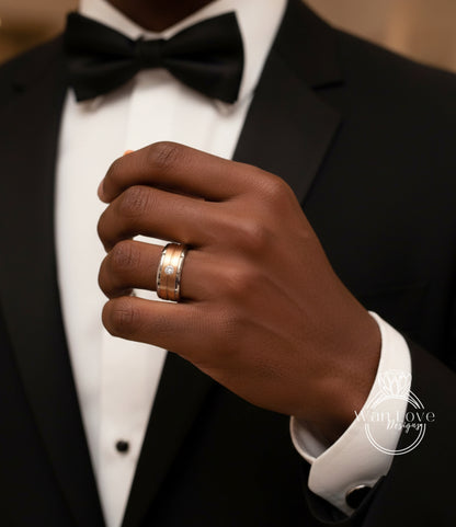 A close-up of a person's hand wearing a gold wedding ring, with a black bow tie and a black tuxedo jacket.
