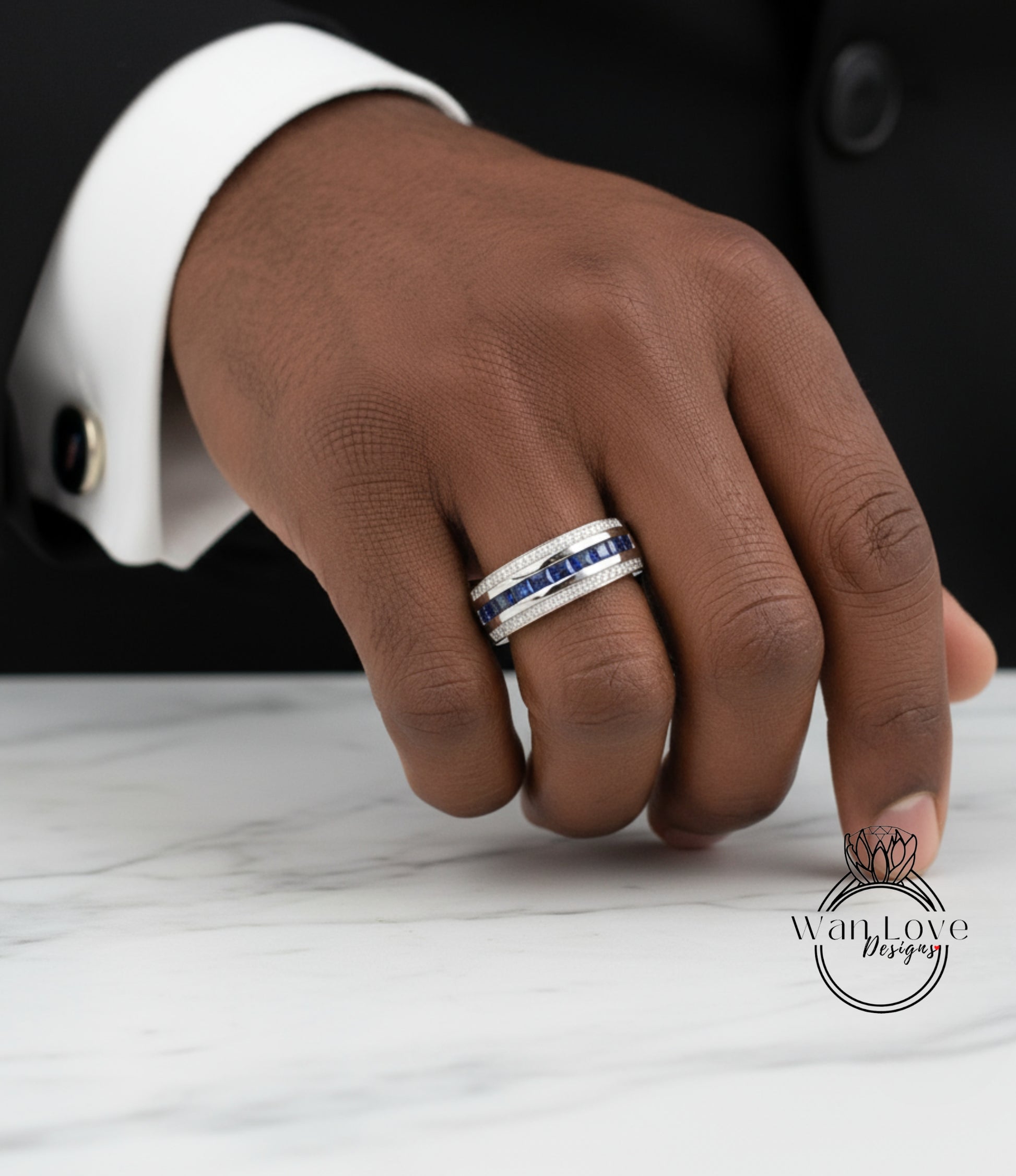 A close-up of a hand wearing a ring with blue and white stones, resting on a marble surface.