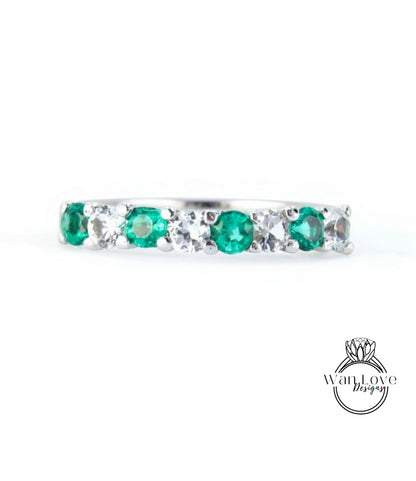 A silver ring with a row of green and white gemstones, including diamonds, set in a band.