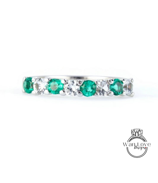 A silver ring with a row of green and white gemstones, including diamonds, set in a band.